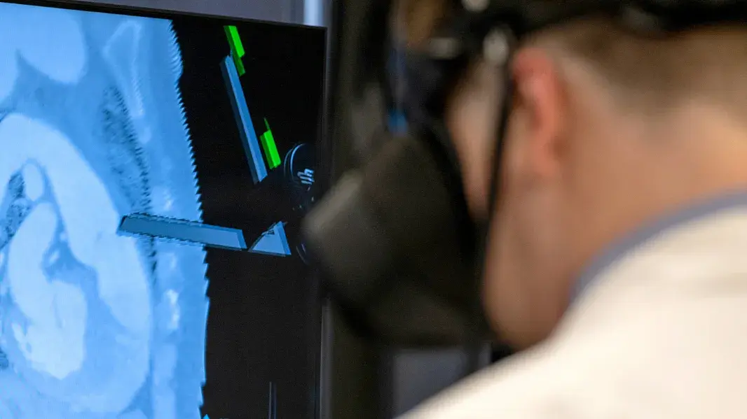 Back of a students head wearing a VR headset in front of a display with anatomical parts.